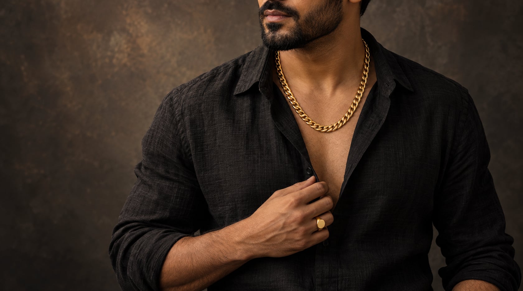 Man in a black linen shirt wearing a gold Cuban-link chain and signet ring