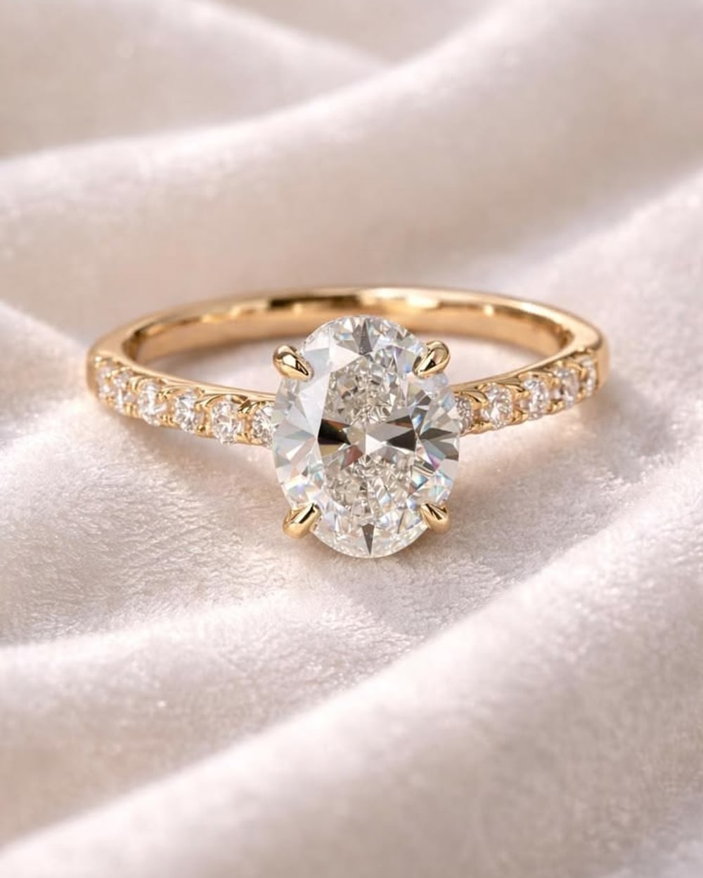 Oval diamond engagement ring with a pavé yellow gold band on ivory velvet
