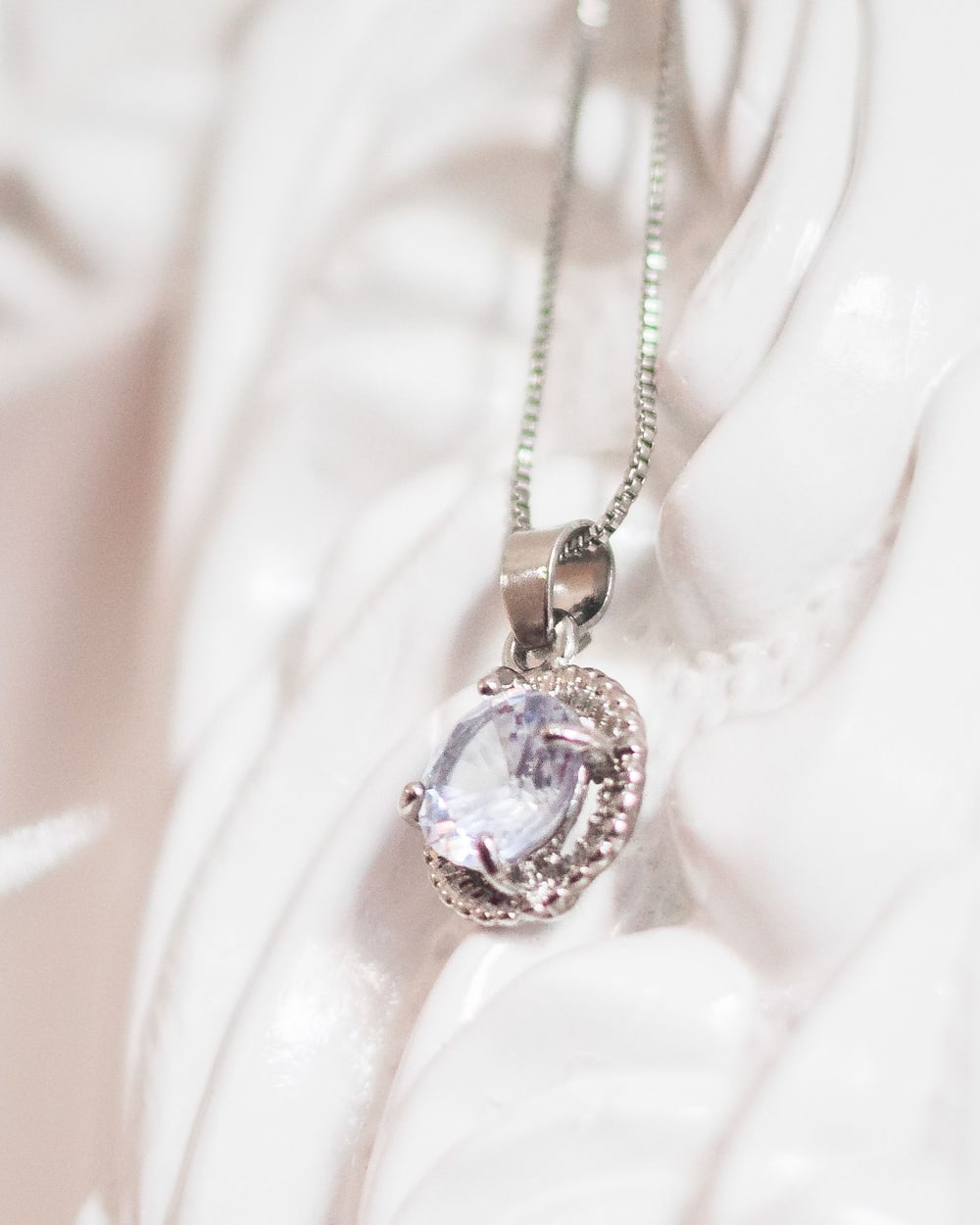 Single diamond pendant on a fine chain against soft ivory
