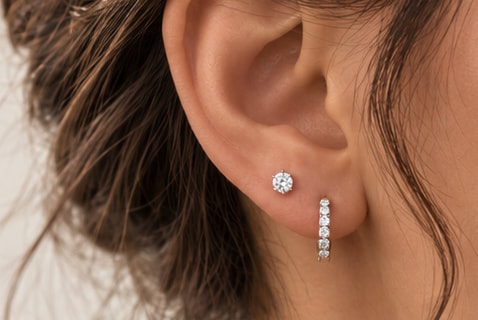 Ear wearing a round diamond stud and a diamond huggie hoop
