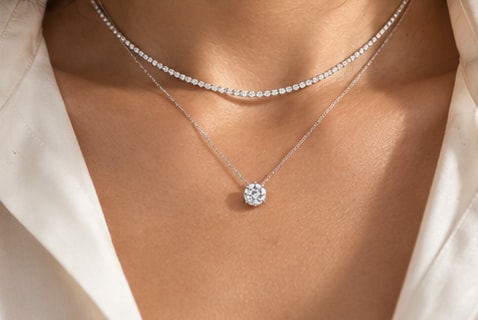 A diamond tennis necklace layered with a round diamond solitaire pendant