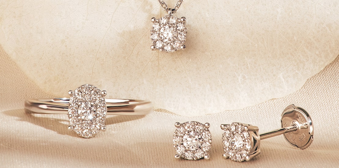 Diamond halo pendant, oval halo ring and round halo stud earrings in white gold on ivory silk
