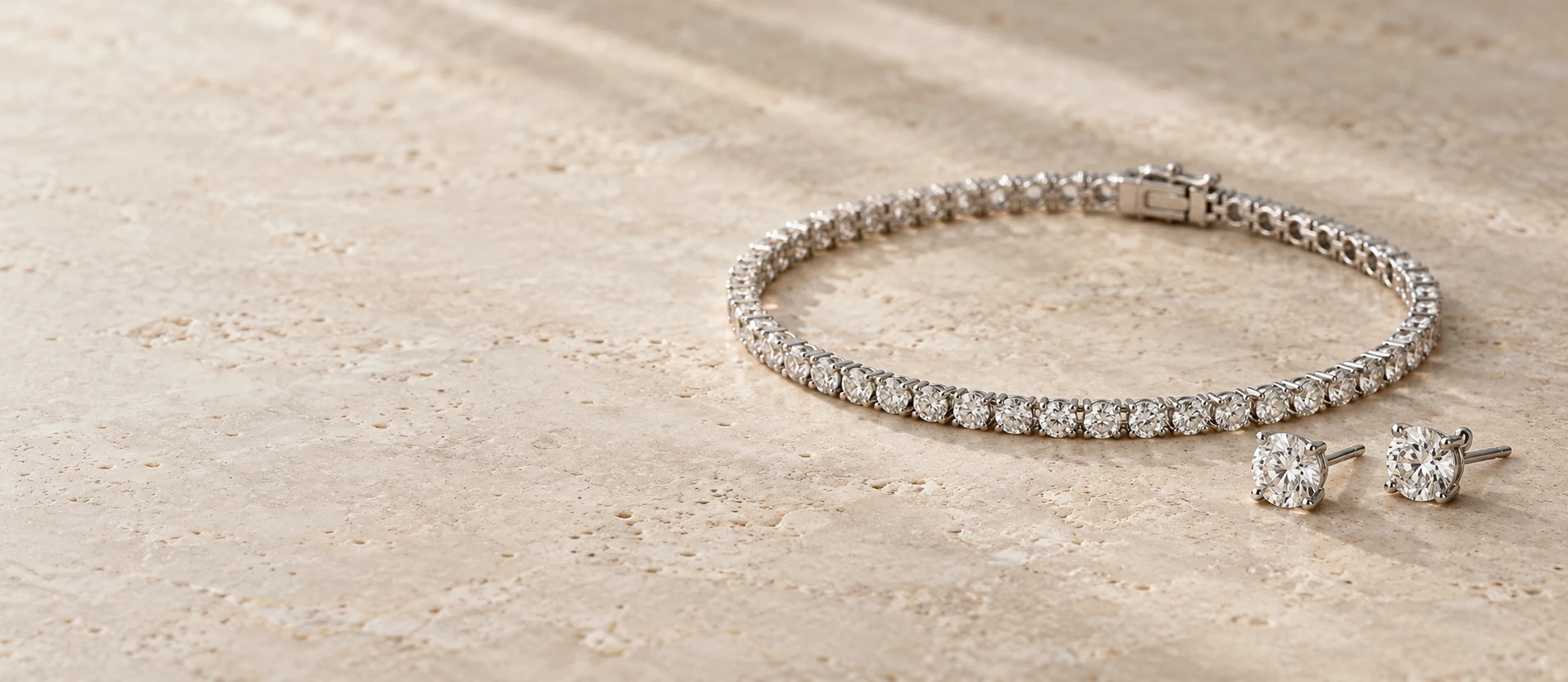 White-gold diamond tennis bracelet and round diamond stud earrings on warm textured limestone in soft daylight