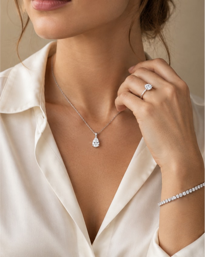 Woman in an ivory silk shirt wearing a pear diamond pendant, a round solitaire ring and a diamond tennis bracelet